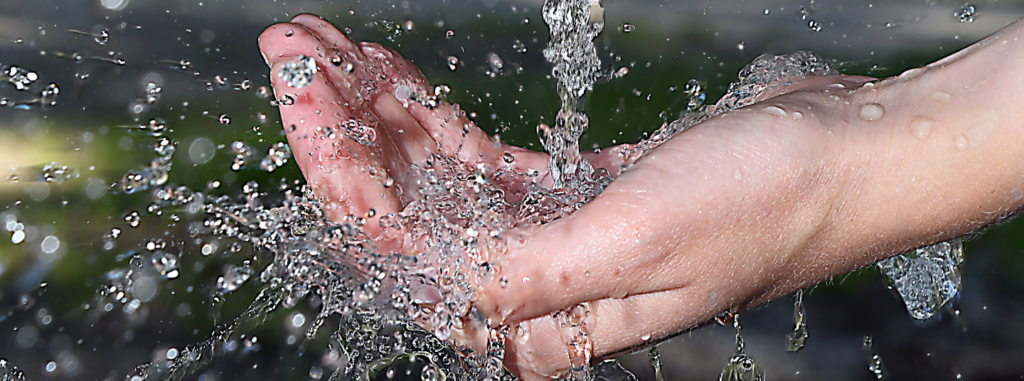 Hand fängt frisches Wasser aus einem Brunnen im Freien auf.