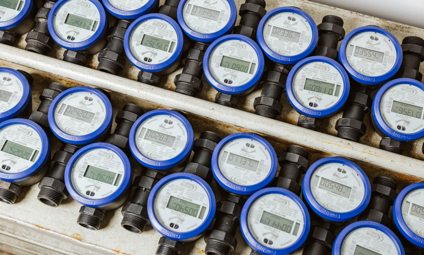 Mehrere aufgereihte Wasserzähler mit digitalen Anzeigen in einer technischen Umgebung.